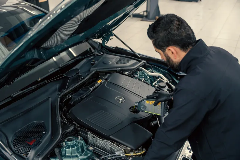 Mechanic topping up the engine oil of a vehicle with the bonnet open