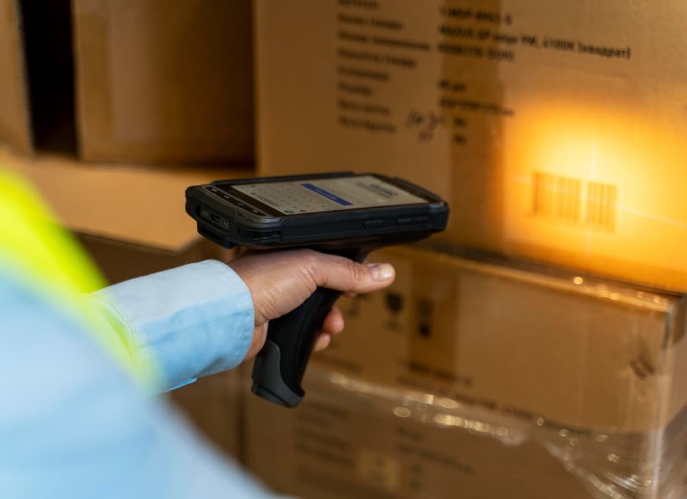 A warehouse worker uses a handheld scanner to scan a barcode on a cardboard box, facilitating inventory management and asset tracking.